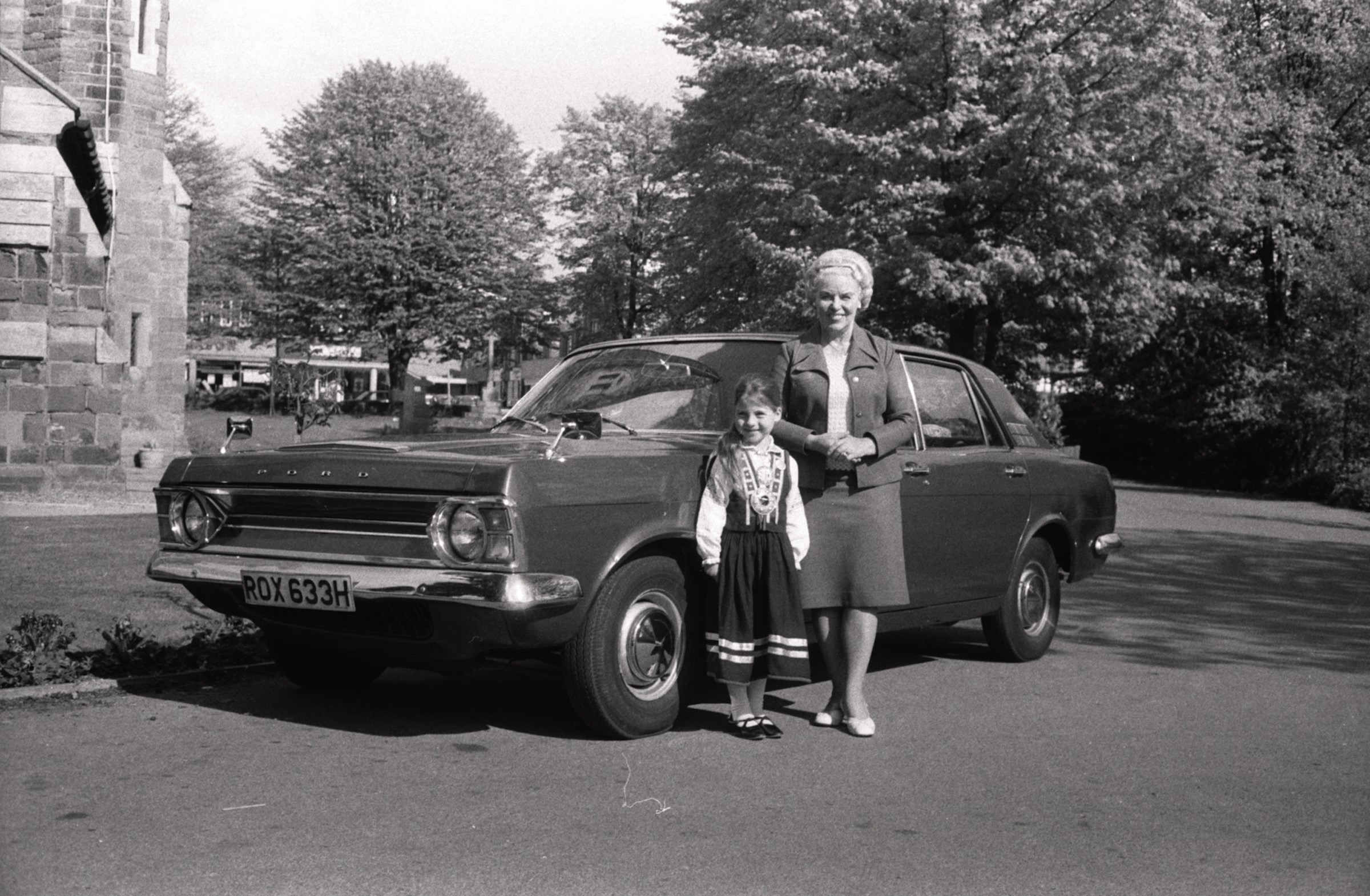 Anita Blezūrs tautas tērpā, Natālija Miķelsons un Harija Blezūra automašīna 'Ford Zephyr' pie Visu Svēto baznīcas Birmingemā, 1972. gads.