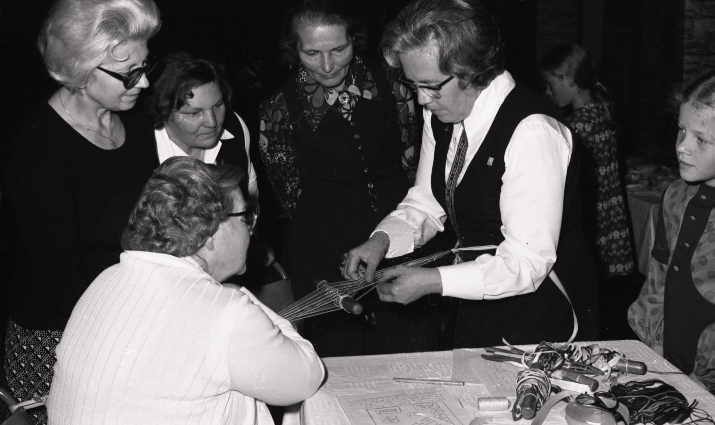 Celu jostas aušana Daugavas vanadžu organizācijas saietā Lesterā, 1974. gads. No labās viena aiz otras mazās māsas Zinta un Māra Ozoliņas, vidū no labās audēja Hermīna Rītiņa, Anna Mūrnieks un Vanda Plūme. Sēž Miklucāns kundze.