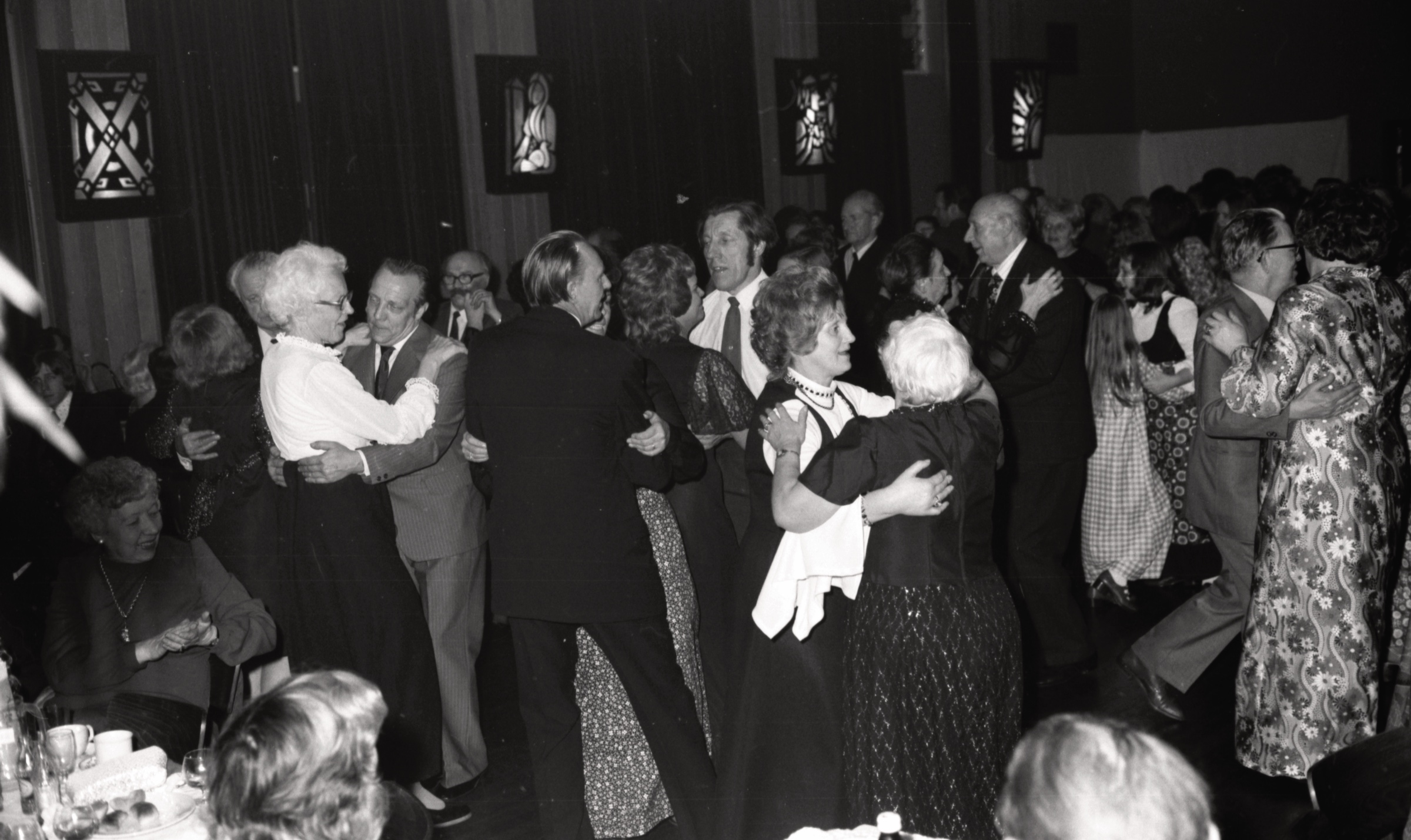 Koventrijas jauktā kora 'Senatne' vakara saviesīgā daļa DVF Koventrijas nodaļas īpašumā 'Mūsmājas', Volstona, Varvikšīra, 1974. gada 26. oktobris. No kr. baltā blūzē Alvīne Pokšāns, centrā baltā kreklā Fricis Laudobelis, viņam priekšā dejo Hilda Krūmiņš un Helga Blīgzna, no viņām pa labi - melnā uzvalkā Kārlis Kazemnieks ar māsu.