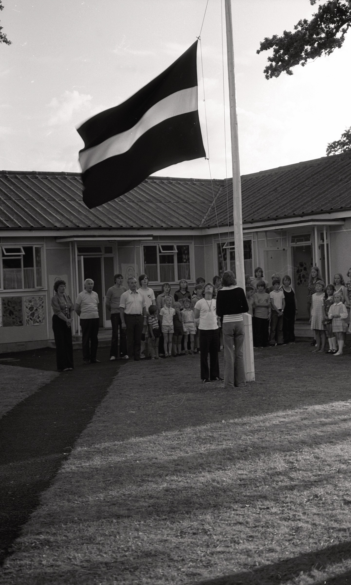 Latvijas karoga pacelšana bērnu nometnē LNPL Latviešu mājā Almelijā, Herefordšīrā, 1975. gads. No kr. nometnes vadītāja Rita Jefimova un diriģents Andrejs Pommers.