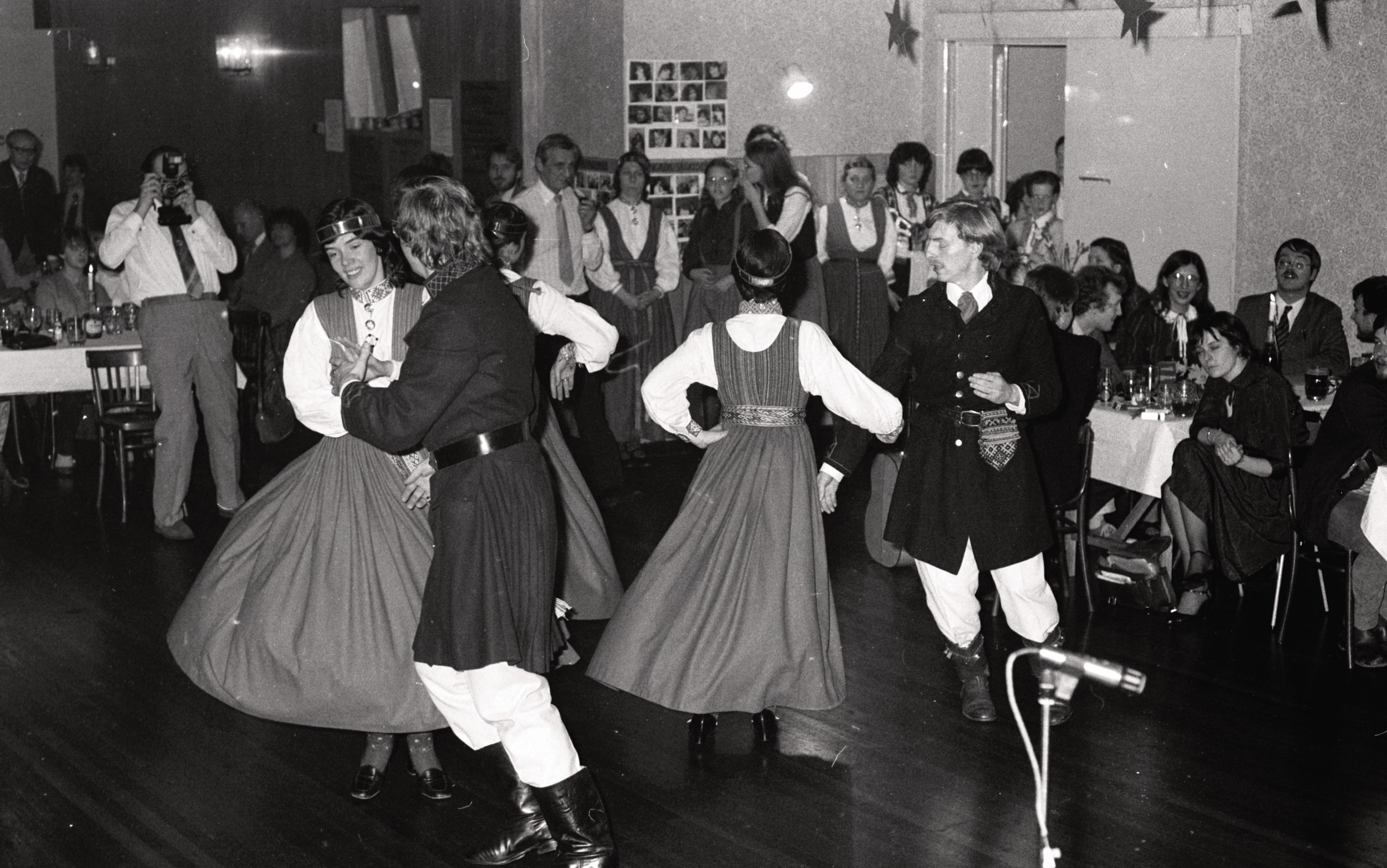 Līdsas latviešu deju kopa 'Kamoliņš' uzstājas Eiropas latviešu jaunatnes apvienības Anglijas nodaļas 'Jautrajā vakarā' DVF namā Bredfordā 1983. gada 19. martā. No kr. ar fotoaparātu Egons Andersons, dejo Inta Dāle un Māris Andersons, Stephanie Dāle un Andrejs Durvards. Aizmugurē vidū stāv no kr. tautas tērpā Mudīte Turciņa, Indra Jefimovs, nezināms, Maija Andersone, Monika Lisovskis, nezināms un Valdis Užāns. Pie galda no labās Andris Bankovskis.